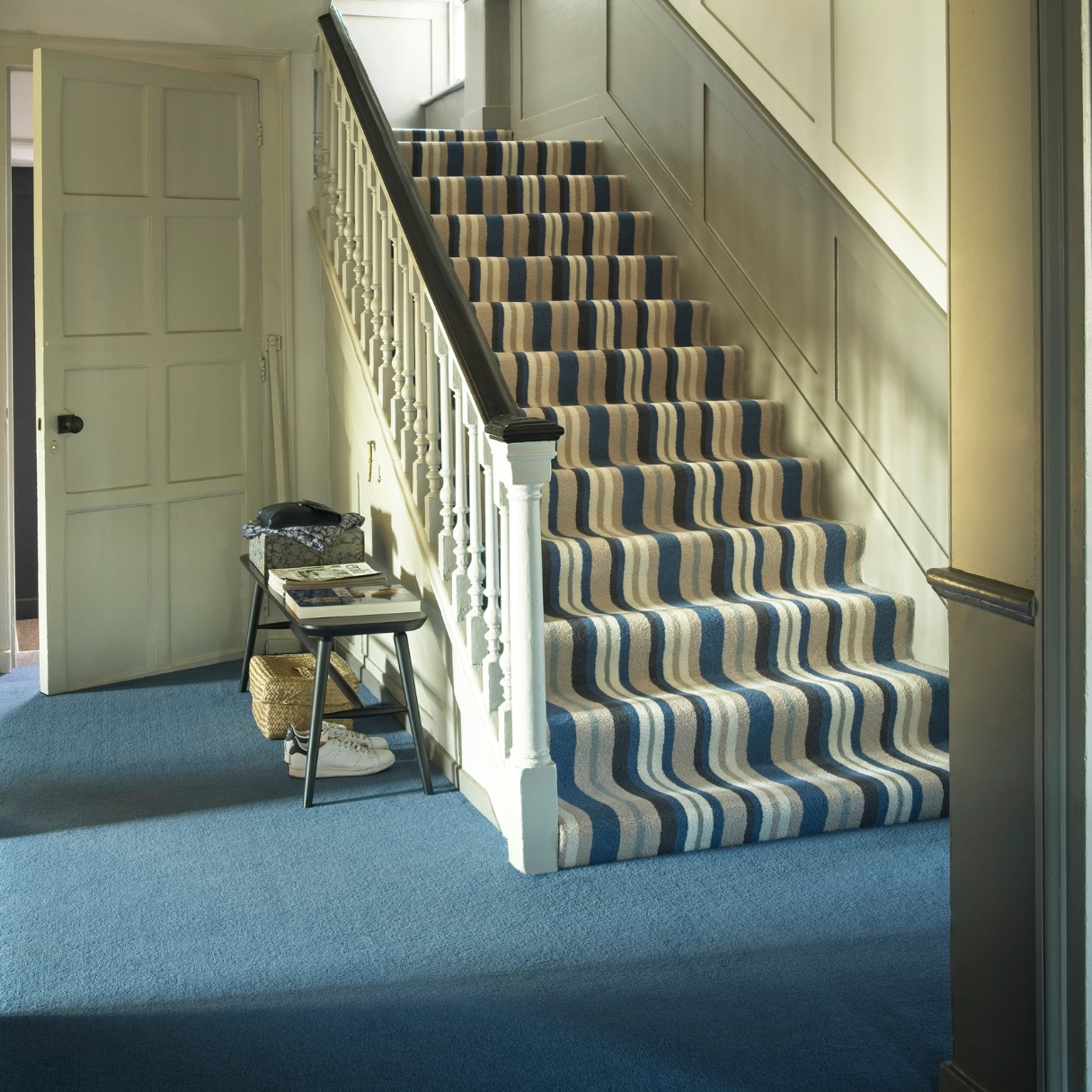 Photo shows a hallway with deep blue carpet and striped carpet stairs
