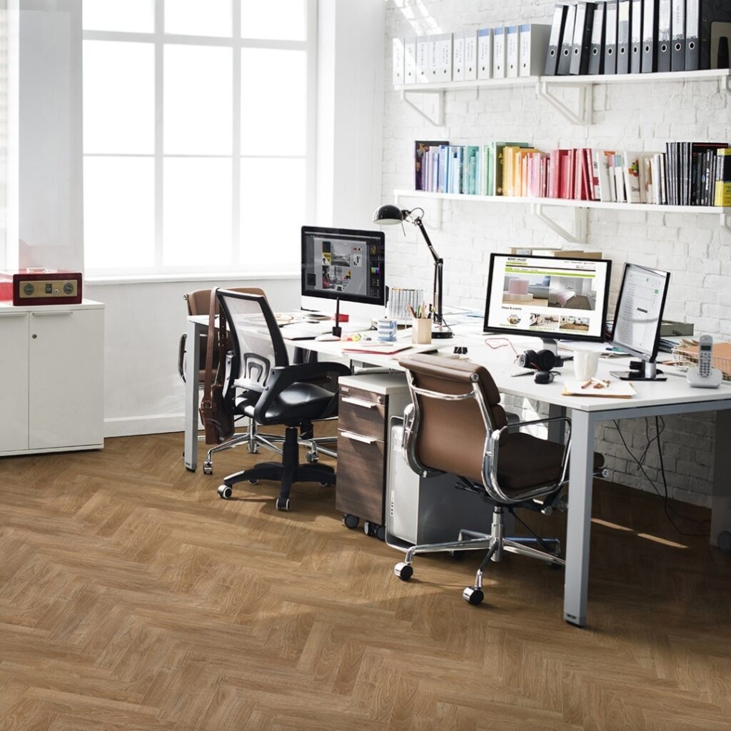 Photo shows an office space with herringbone style laminate flooring. Laminate flooring is available at Wall Bros in Worthing and Storrington