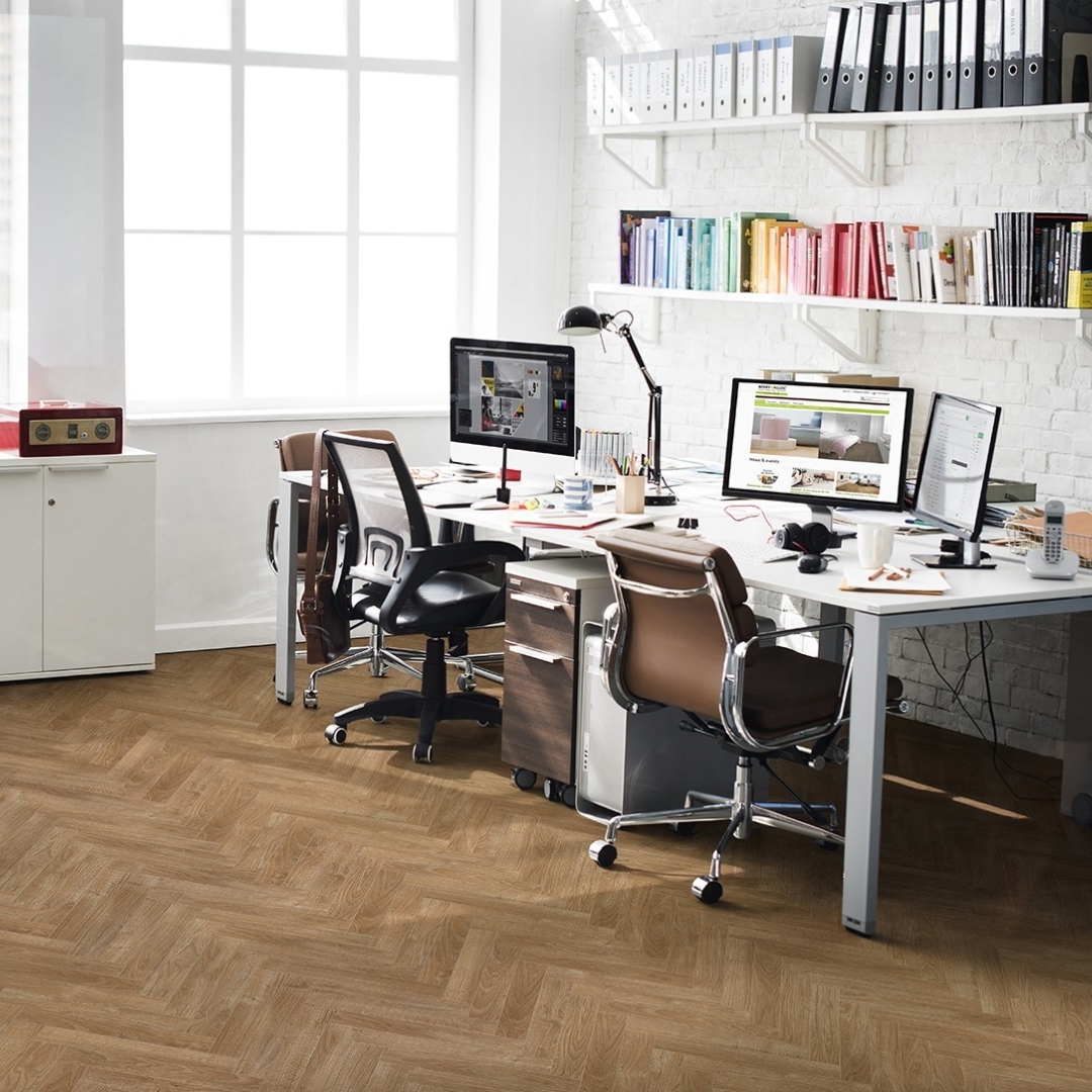 Photo shows an office space with herringbone style laminate flooring. Laminate flooring is available at Wall Bros in Worthing and Storrington